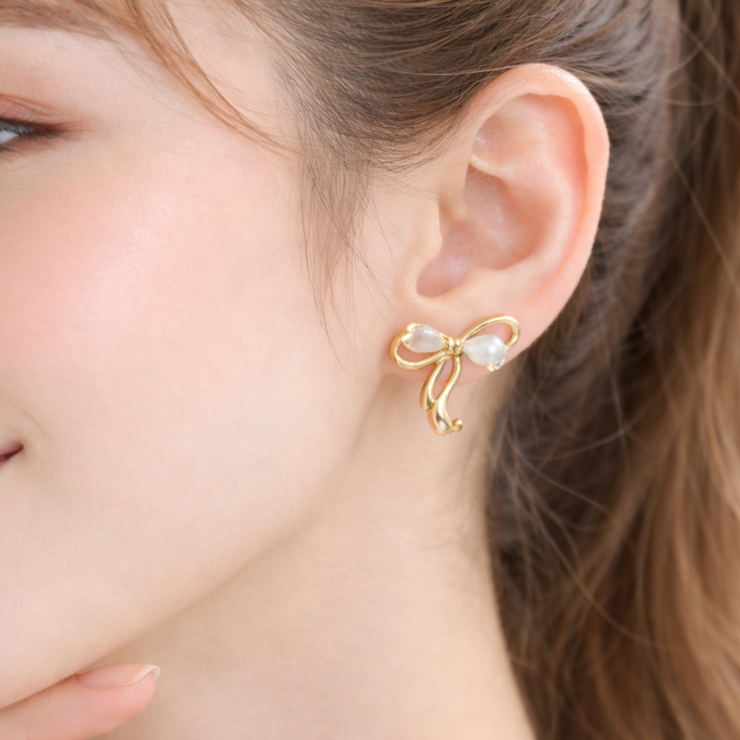 Gold bow stud earrings with teardrop pearl accents on white background