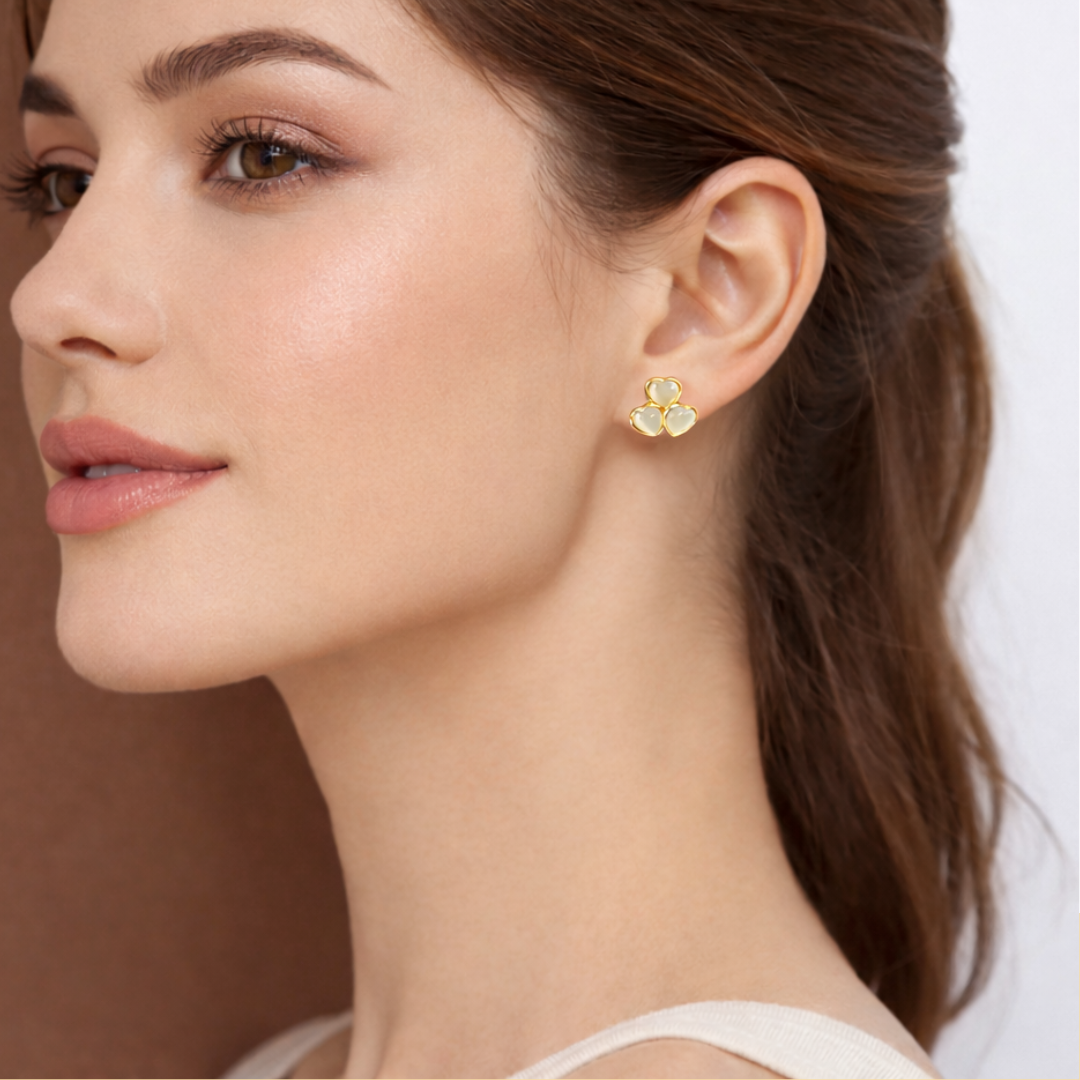 Elegant woman wearing small gold clover earrings with natural makeup and soft lighting close-up portrait.