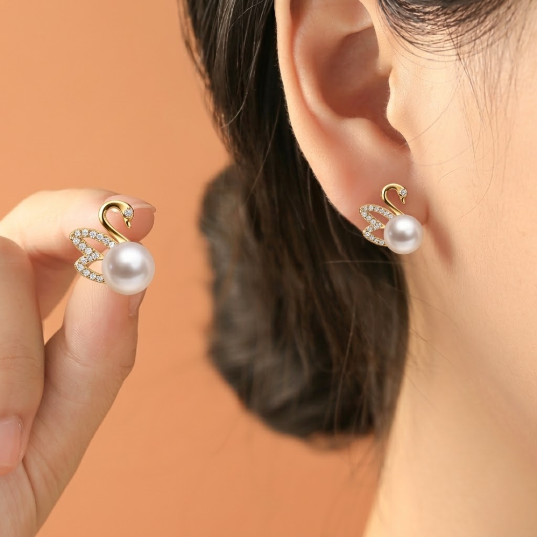 Gold swan pearl earrings with rhinestones held in hand